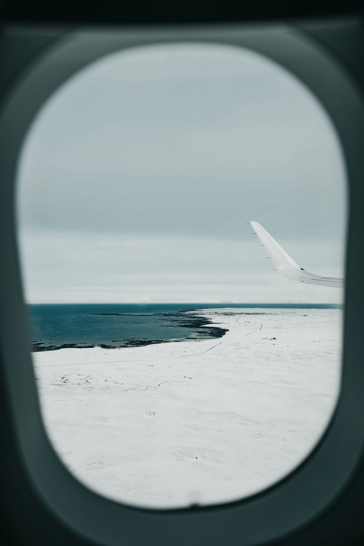 A winglet over a snowy coastline, seen through a cabin window